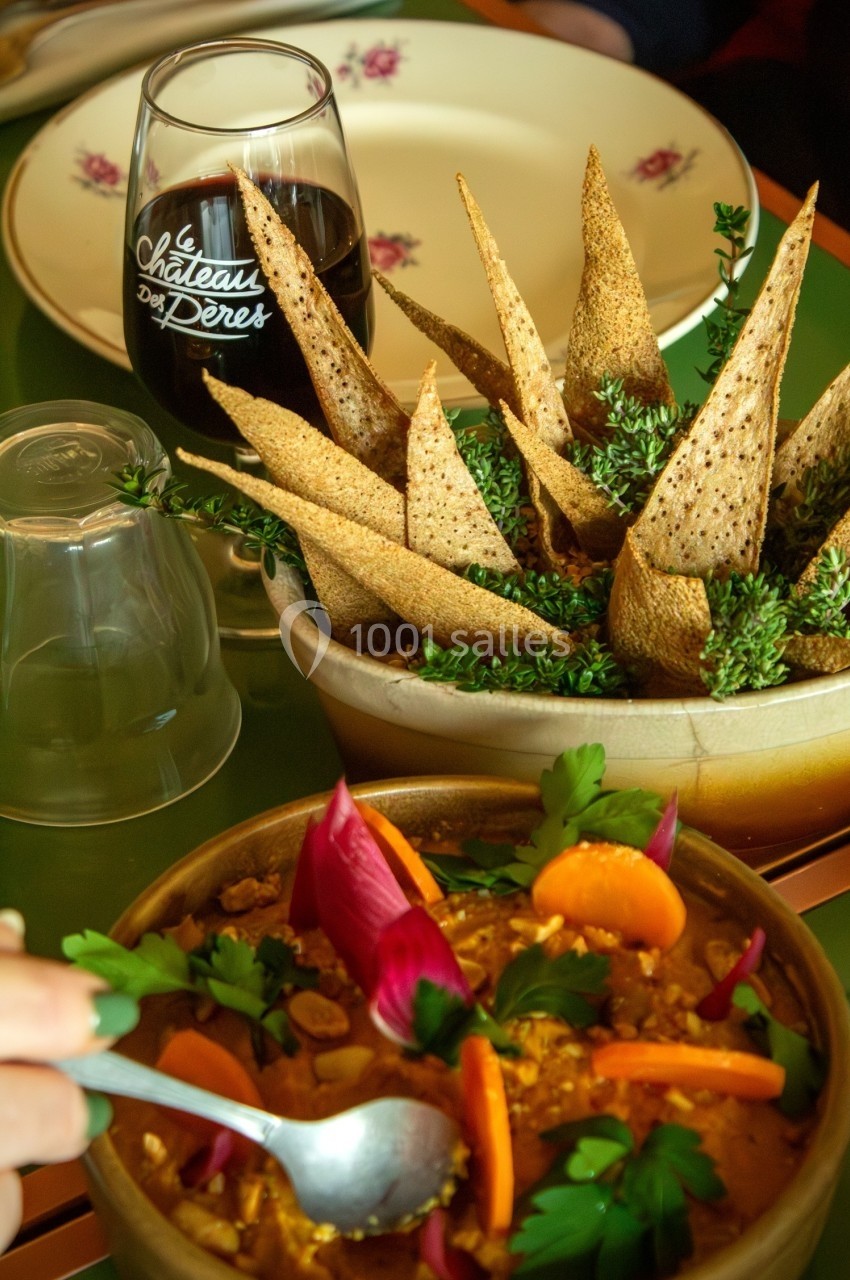 Assiette de houmous décorée de légumes colorés, accompagnée de pain pita et d'un verre de vin rouge.