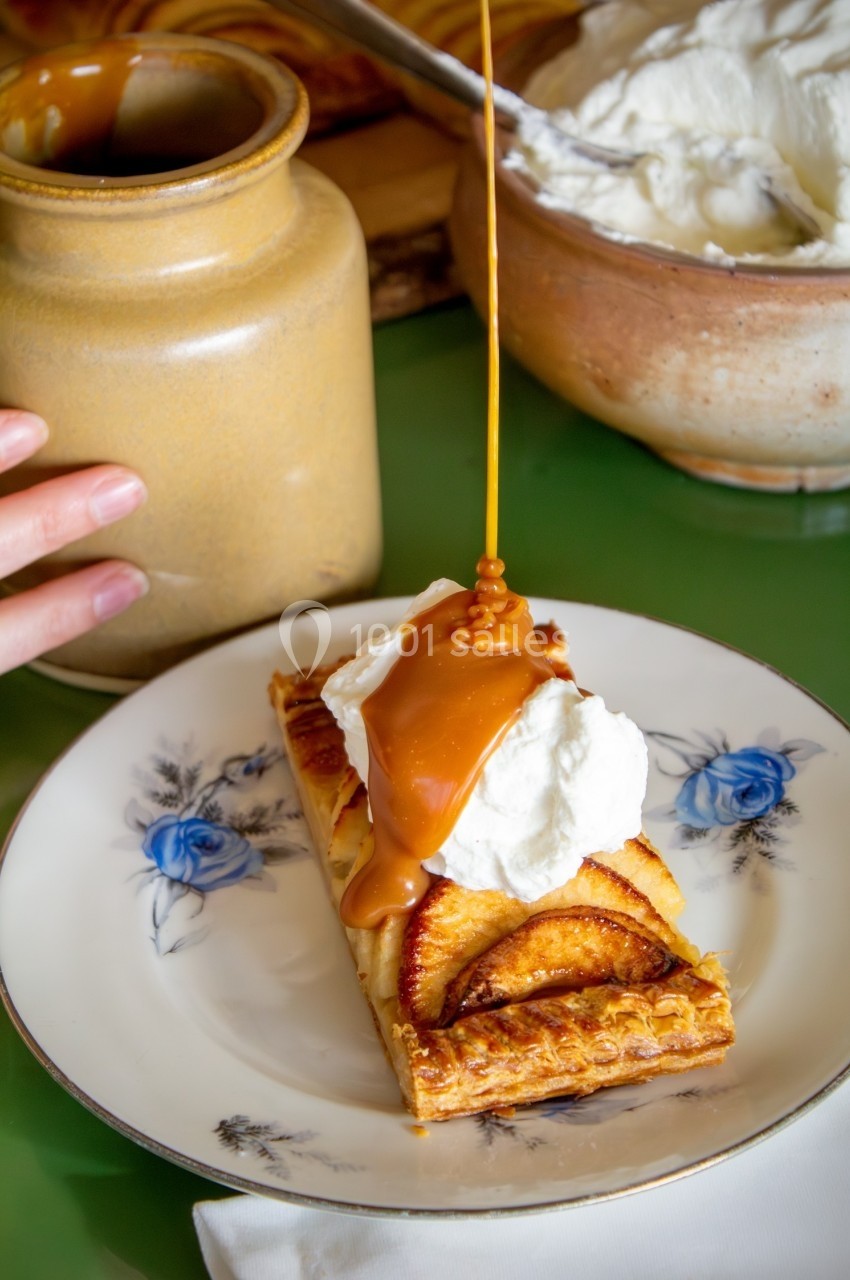 Tarte aux pommes garnie de crème fouettée, nappée de caramel liquide, servie sur une assiette décorée.