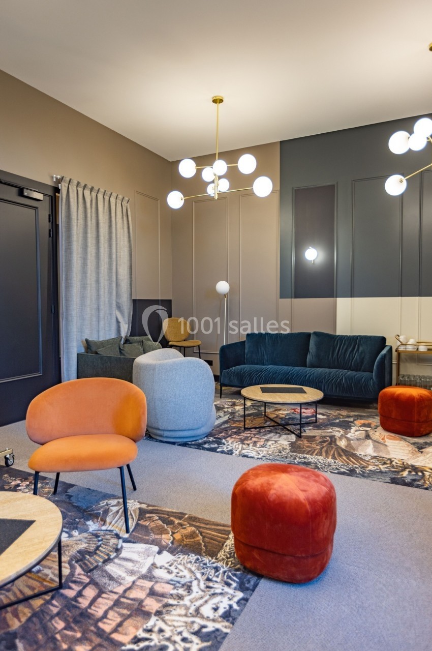 Salon moderne avec fauteuils colorés, canapé bleu, tables basses en bois et luminaires suspendus dans un décor chaleureux.