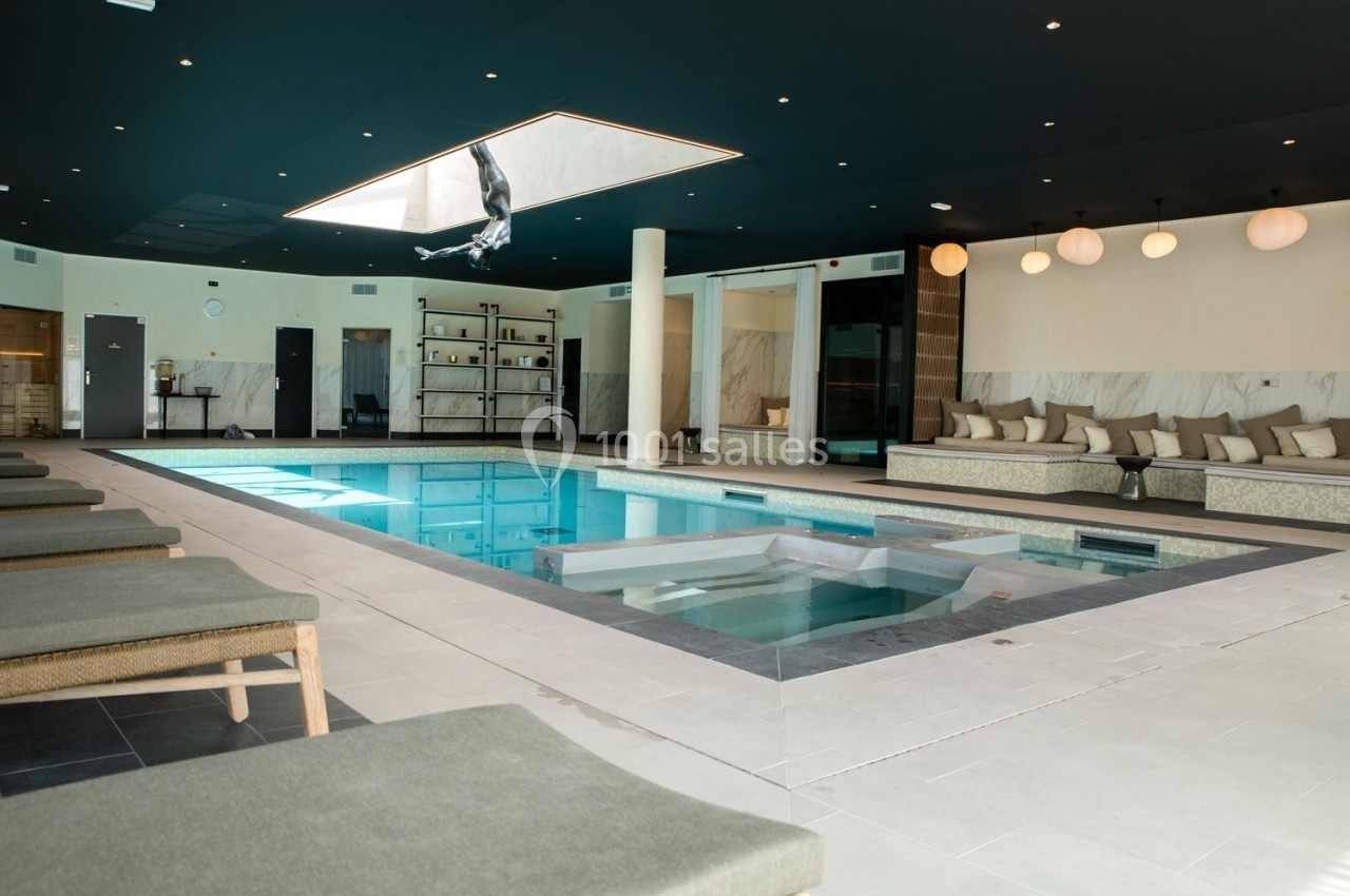 Piscine intérieure moderne avec bain à remous, chaises longues et éclairage tamisé dans un espace élégant.