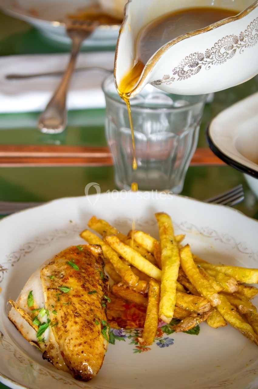 Poulet rôti avec des frites dorées, servi dans une assiette, accompagné d'une sauce versée depuis une saucière.