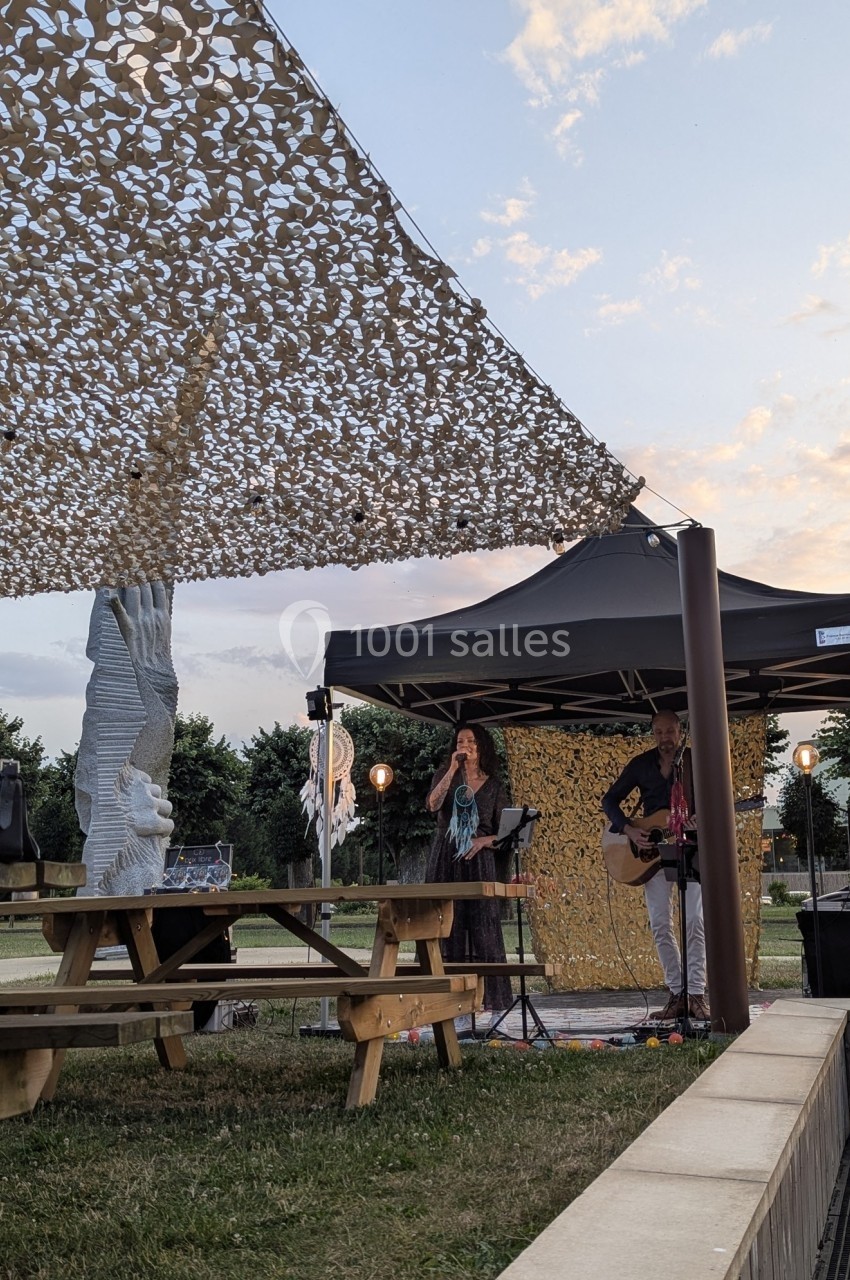 Deux musiciens jouent sous un chapiteau en plein air, près de tables de pique-nique et d'une décoration suspendue.