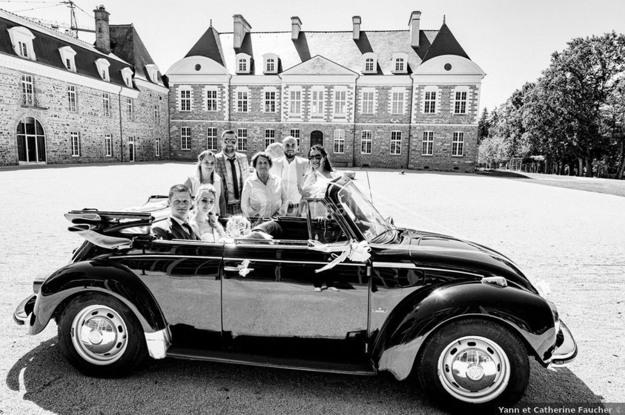 Un groupe de personnes posant dans une voiture décapotable ancienne devant un grand bâtiment historique.