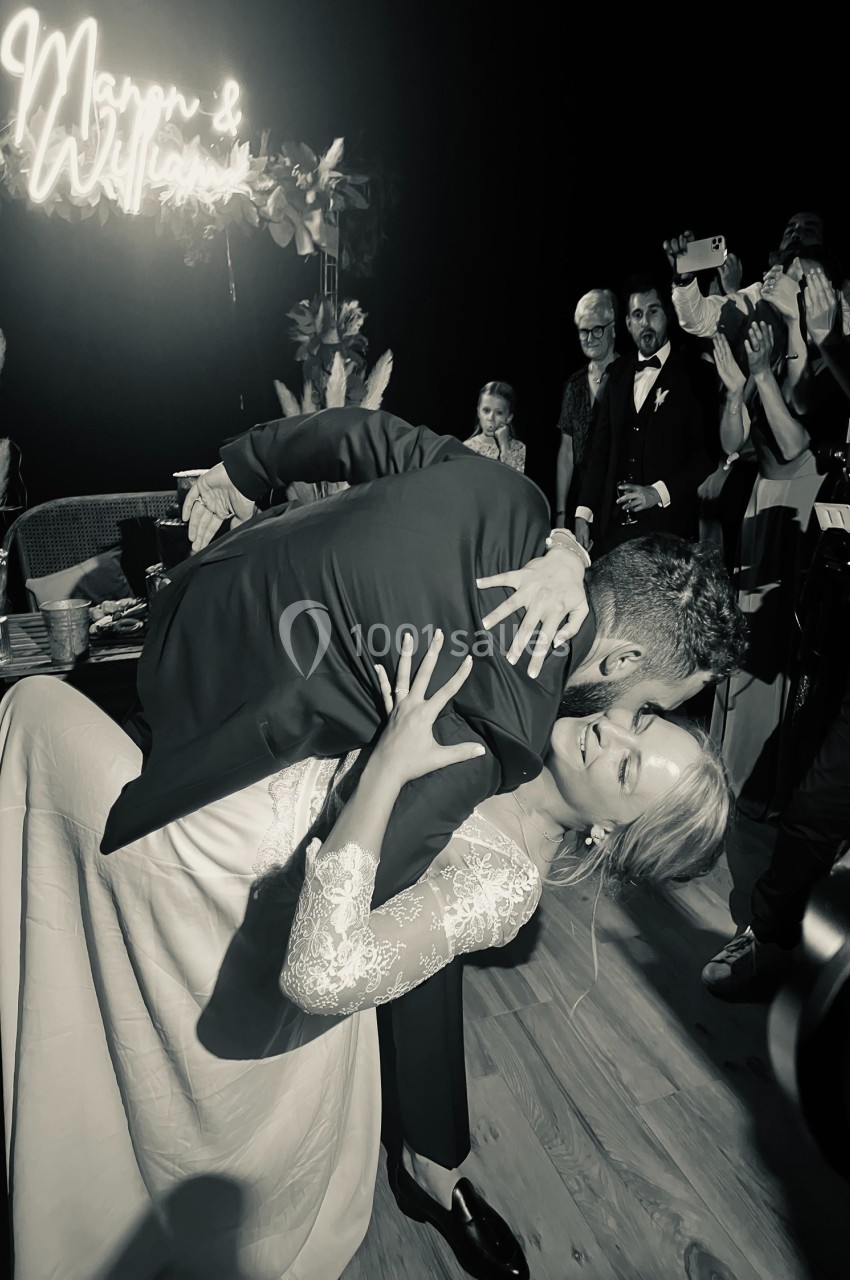 Un couple danse, l'homme penche la femme en arrière dans une salle sombre avec des invités en arrière-plan.