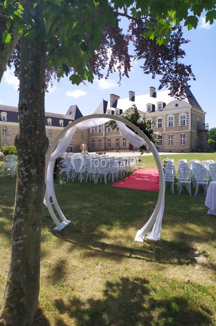 Arche décorée en tissu blanc devant des chaises alignées et un château en arrière-plan, lors d'une cérémonie en extérieur.