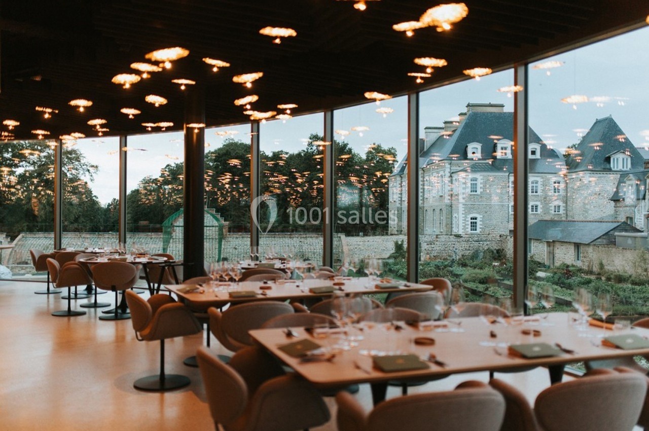 Salle de restaurant moderne avec grandes baies vitrées offrant une vue sur un bâtiment historique et un jardin.