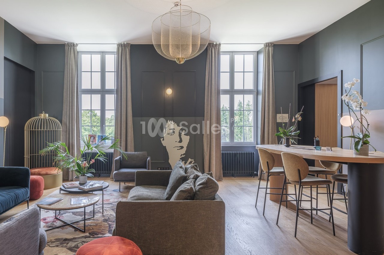 Salon moderne avec canapés, table basse, bar, grandes fenêtres, murs sombres et décoration végétale.