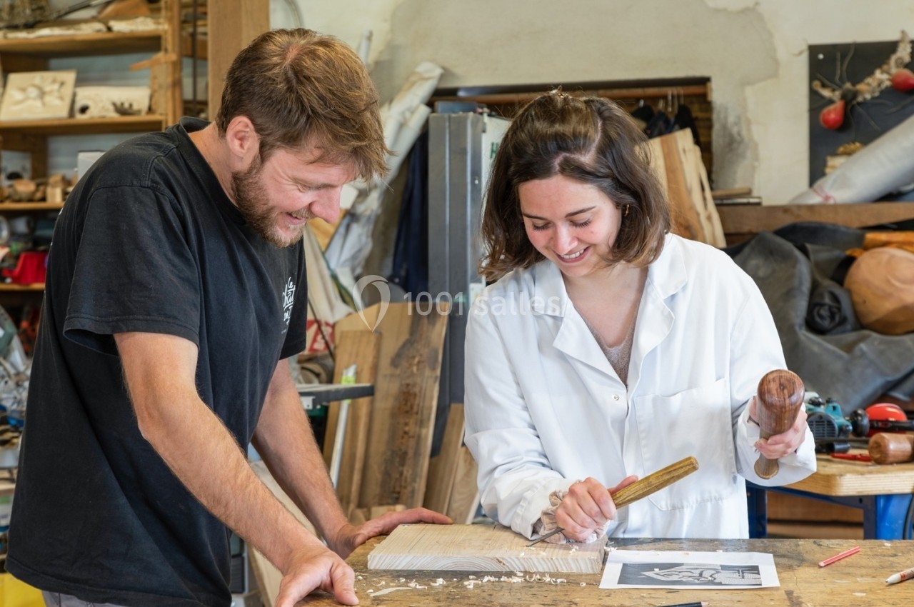 Un homme et une femme sculptent du bois ensemble dans un atelier, entourés d'outils et de matériaux.