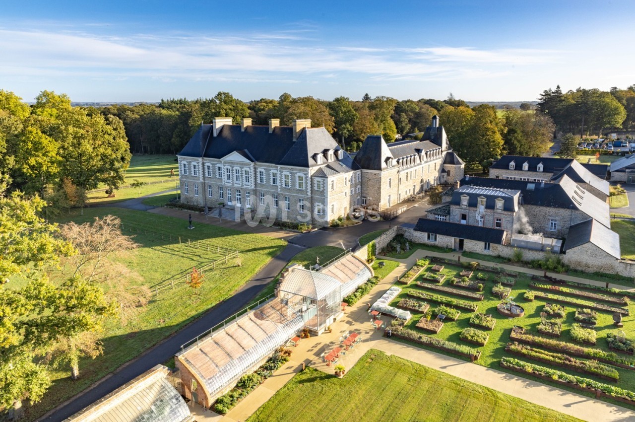 Vue aérienne d'un château entouré de jardins aménagés, de serres et d'espaces verts sous un ciel dégagé.