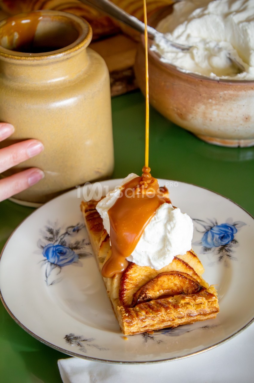 Tarte aux pommes servie avec une cuillère de crème fouettée, nappée de caramel liquide.