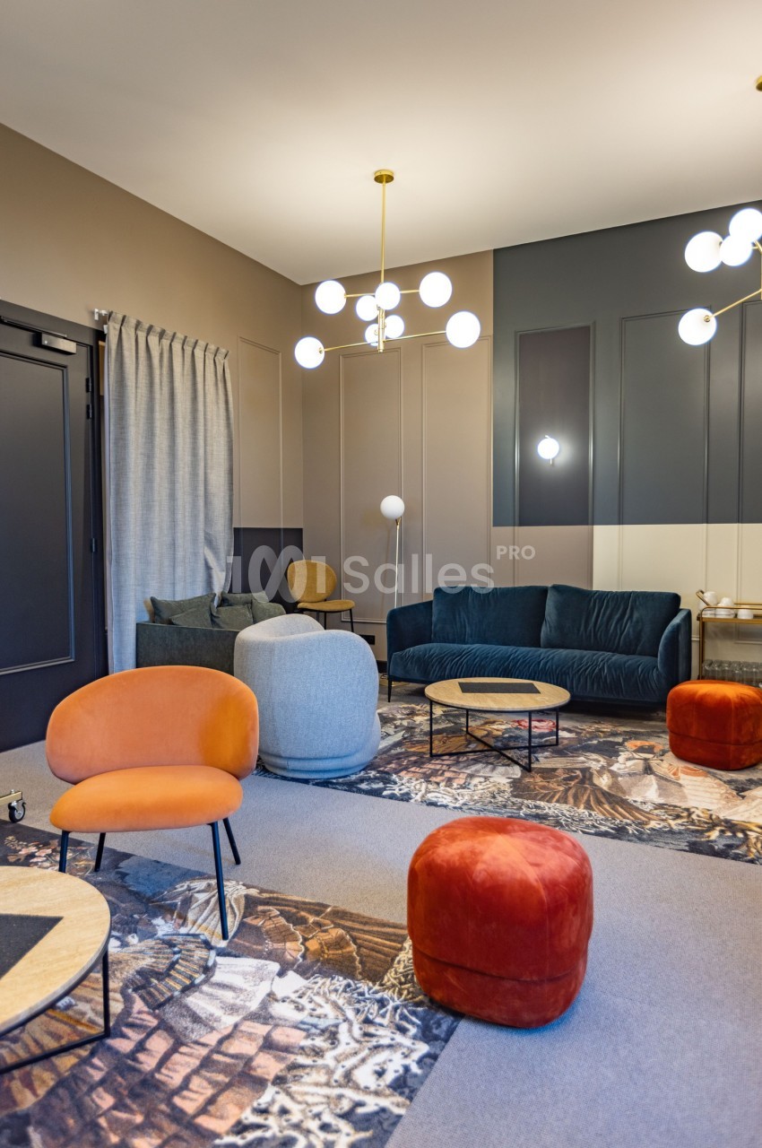 Salon moderne avec fauteuils colorés, canapé vert, tables basses en bois et luminaires suspendus dans un décor chaleureux.