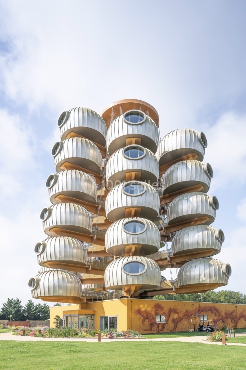 Immeuble moderne avec des balcons circulaires en métal, sur une base jaune, entouré de pelouse et d'arbres.
