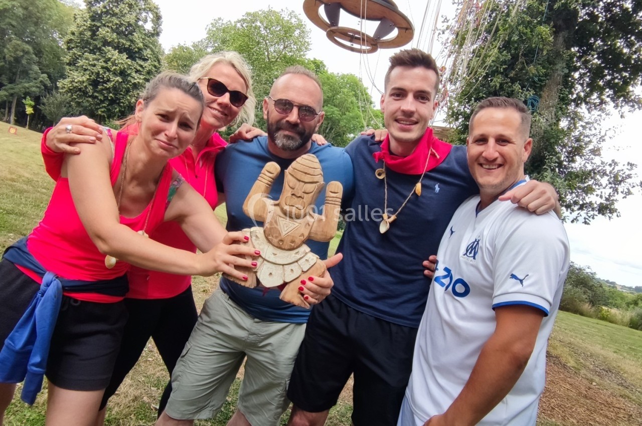 Cinq personnes souriantes posent ensemble dans un parc, tenant une sculpture en bois devant elles.