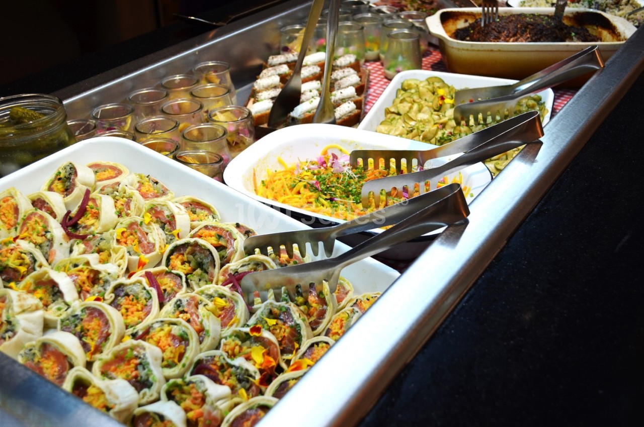 Buffet avec plats variés, incluant rouleaux de légumes, salade colorée, gratin et desserts en arrière-plan.