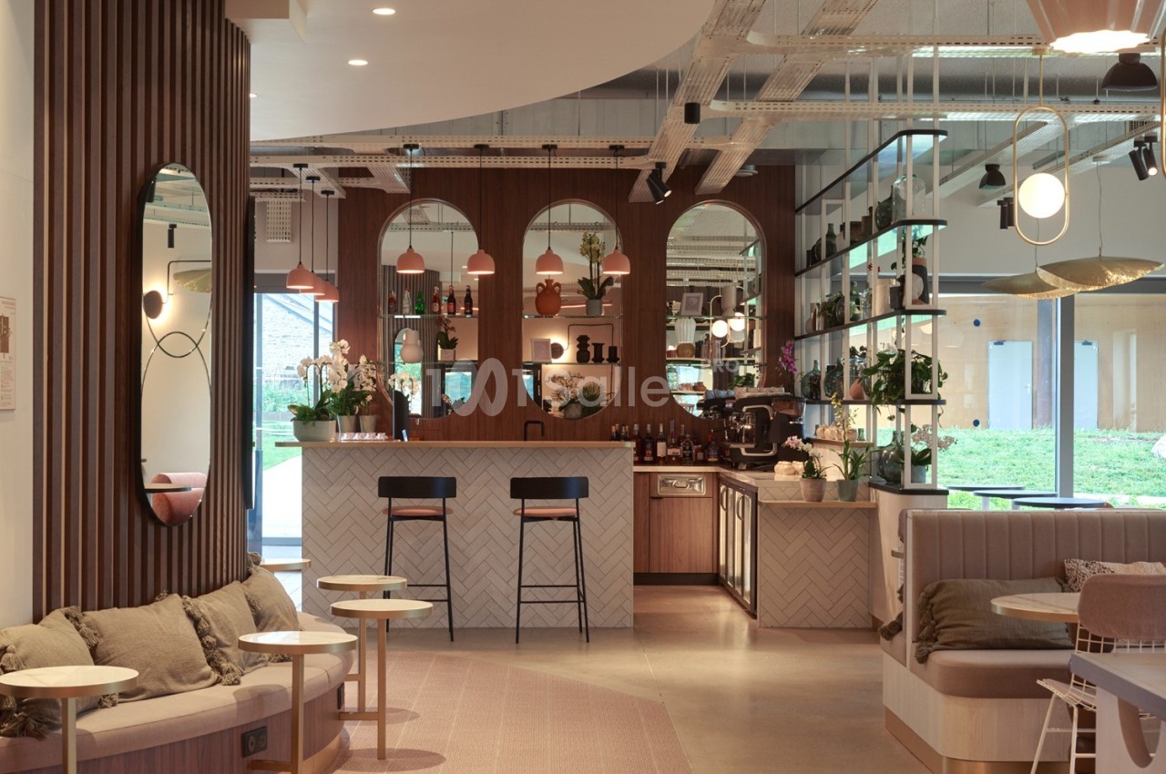 Espace intérieur moderne avec un bar central, des tables, des miroirs et une décoration chaleureuse en bois et tons neutres.