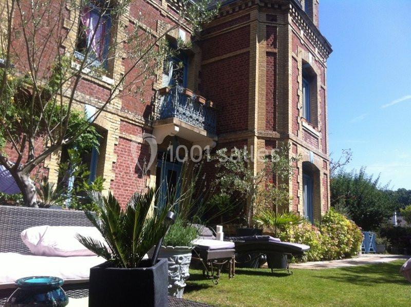 Façade en briques rouges d'une maison ancienne avec balcon, entourée d'un jardin aménagé et de mobilier extérieur.