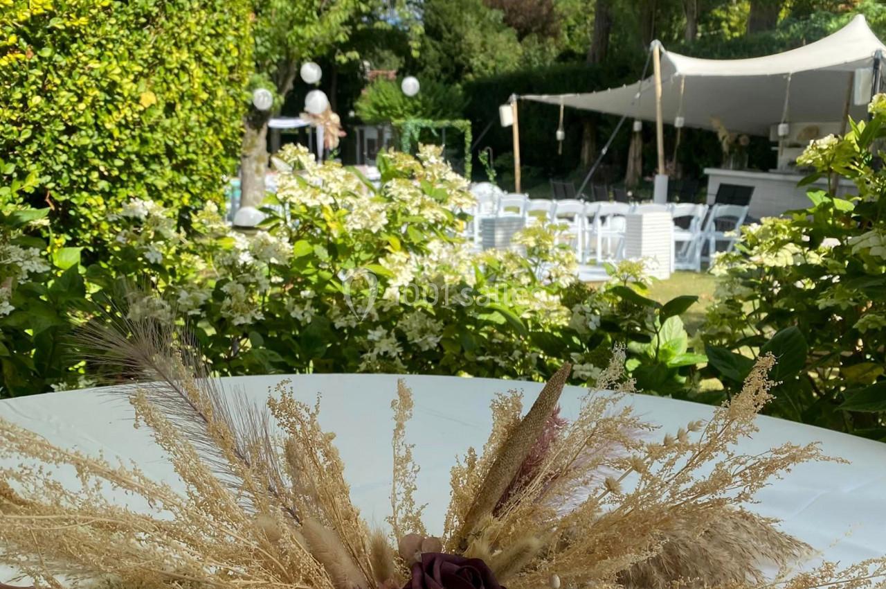 Décoration florale séchée sur une table, avec un jardin verdoyant et une tente blanche en arrière-plan.