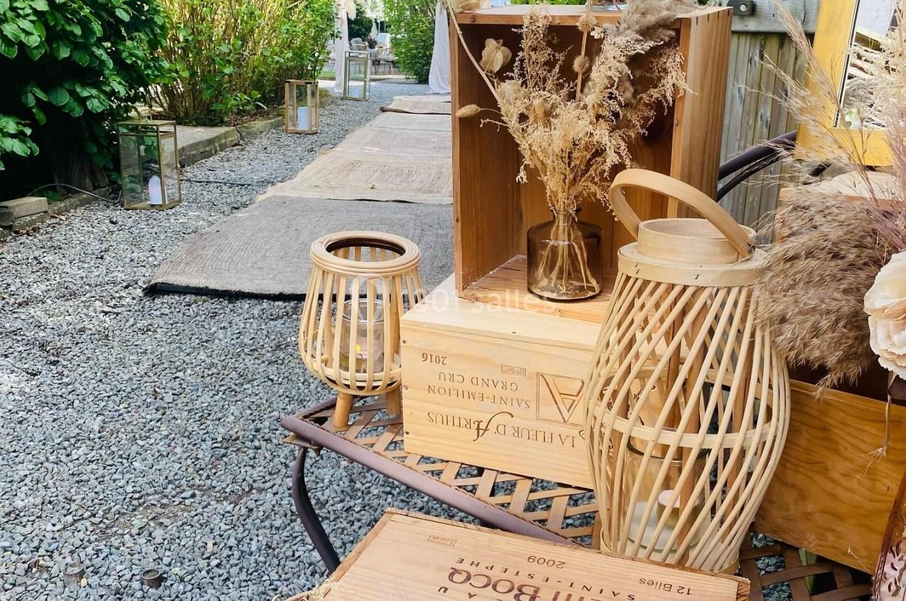 Décoration champêtre avec caisses en bois, lanternes en osier et fleurs séchées sur un chemin de gravier bordé de verdure.