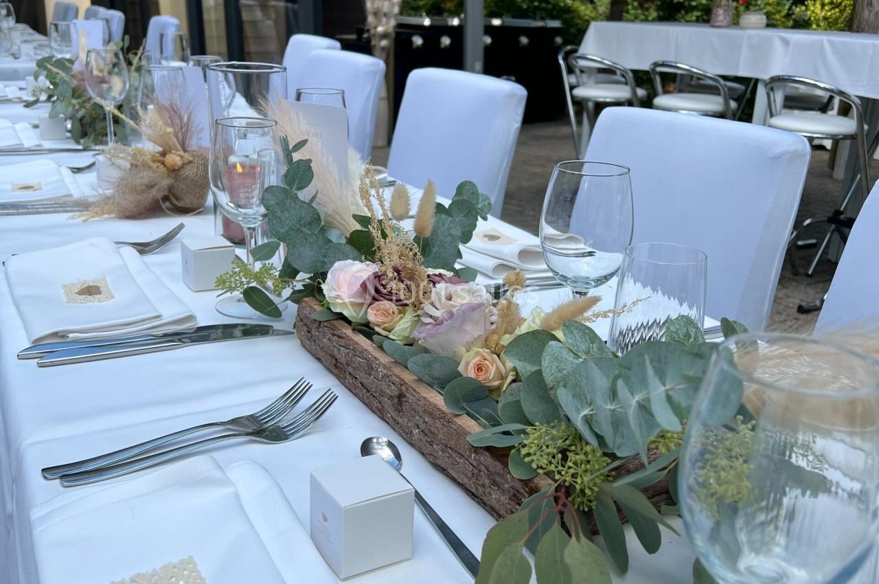 Table dressée pour un événement, décorée avec des fleurs pastel, des feuillages et des éléments naturels dans un cadre…