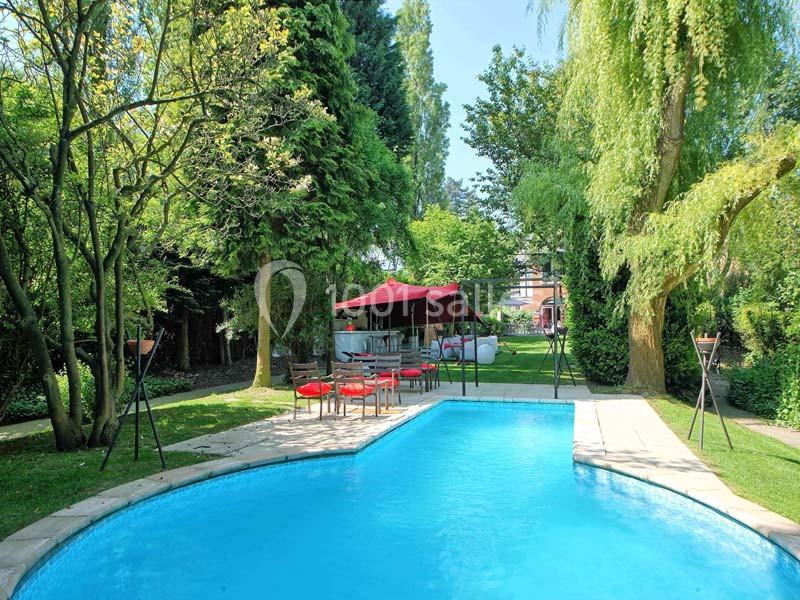 Piscine extérieure entourée de verdure avec un espace détente abrité par une tente rouge au fond du jardin.
