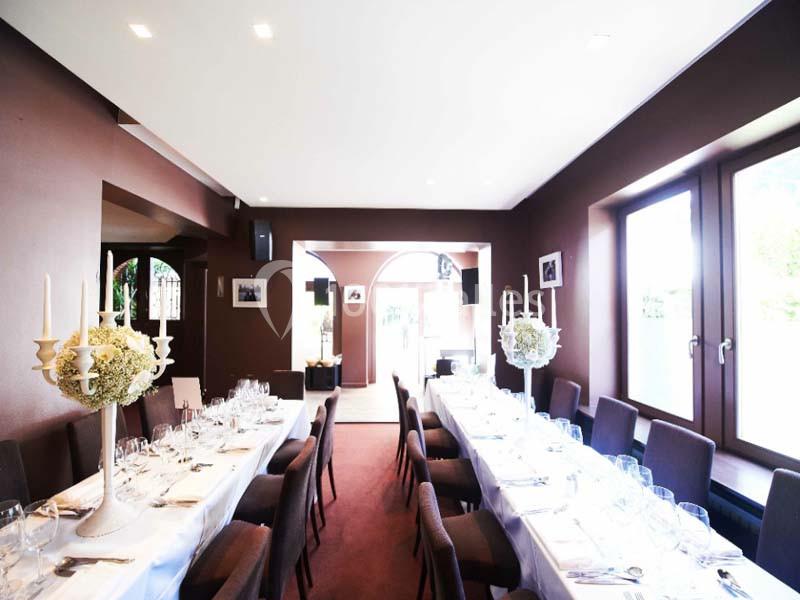 Salle de réception lumineuse avec deux longues tables dressées, décorées de chandeliers et de fleurs blanches.