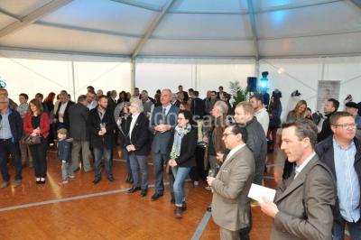 Tente blanche installée sur une pelouse, accueillant un événement avec des invités debout autour de tables hautes.