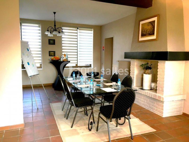 Salle de réunion avec table en verre, chaises noires, tableau blanc, bouteilles d'eau et cheminée en arrière-plan.