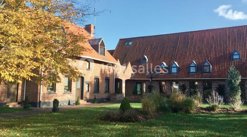 Bâtiment en briques rouges avec toit en tuiles, entouré d'arbres et de pelouse sous un ciel dégagé.