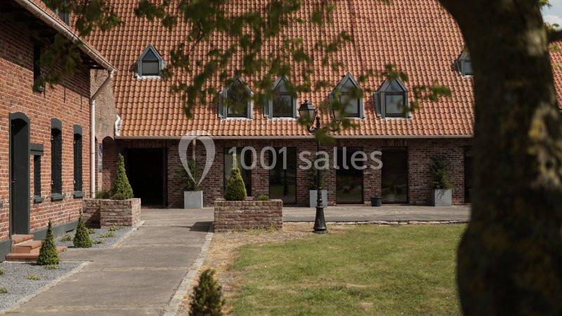 Cour intérieure d'une bâtisse en briques rouges avec toit en tuiles, entourée de végétation et de petits arbustes.