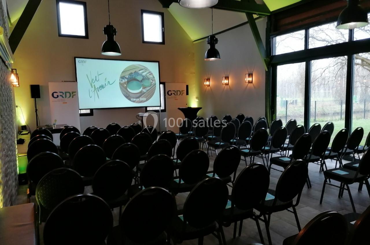 Salle de conférence aménagée avec des rangées de chaises, un écran de projection allumé et des logos GRDF visibles.