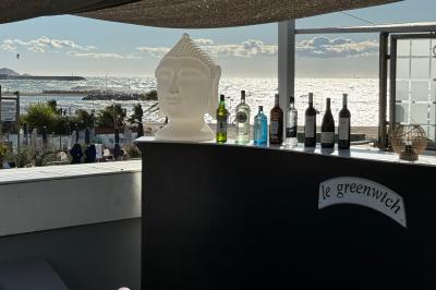Miniature Location salle Marseille (Bouches-du-Rhône) - Le Greenwich #2 Salle de restaurant lumineuse avec tables dressées, chaises noires et blanches, et terrasse extérieure avec vue sur des…