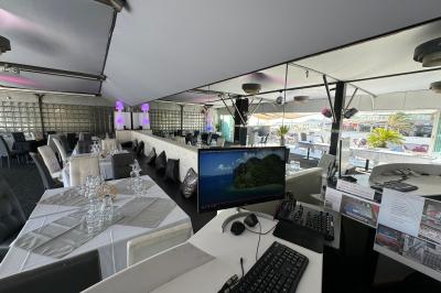 Miniature Location salle Marseille (Bouches-du-Rhône) - Le Greenwich #9 Salle de restaurant lumineuse avec tables dressées, chaises noires et blanches, et terrasse extérieure avec vue sur des…