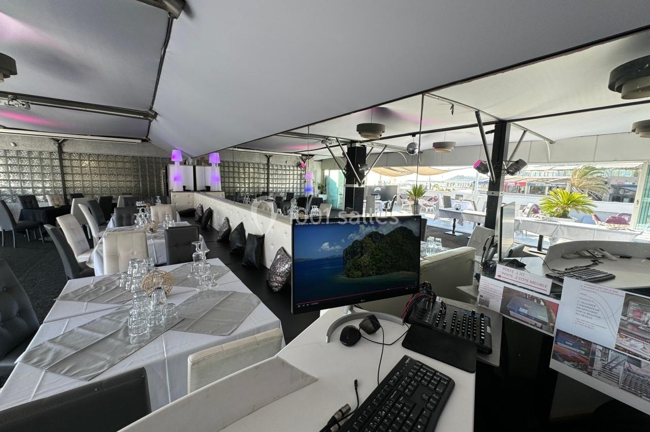 Salle de restaurant lumineuse avec tables dressées, vue sur une terrasse extérieure et un poste informatique au premier plan.