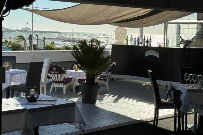 Miniature Location salle Marseille (Bouches-du-Rhône) - Le Greenwich #13 Salle de restaurant lumineuse avec tables dressées, chaises noires et blanches, et terrasse extérieure avec vue sur des…