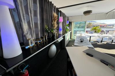 Miniature Location salle Marseille (Bouches-du-Rhône) - Le Greenwich #14 Salle de restaurant lumineuse avec tables dressées, chaises noires et blanches, et terrasse extérieure avec vue sur des…