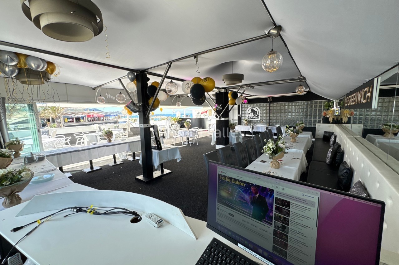 Salle décorée pour un événement avec ballons noirs et dorés, tables dressées et vue sur une terrasse extérieure.