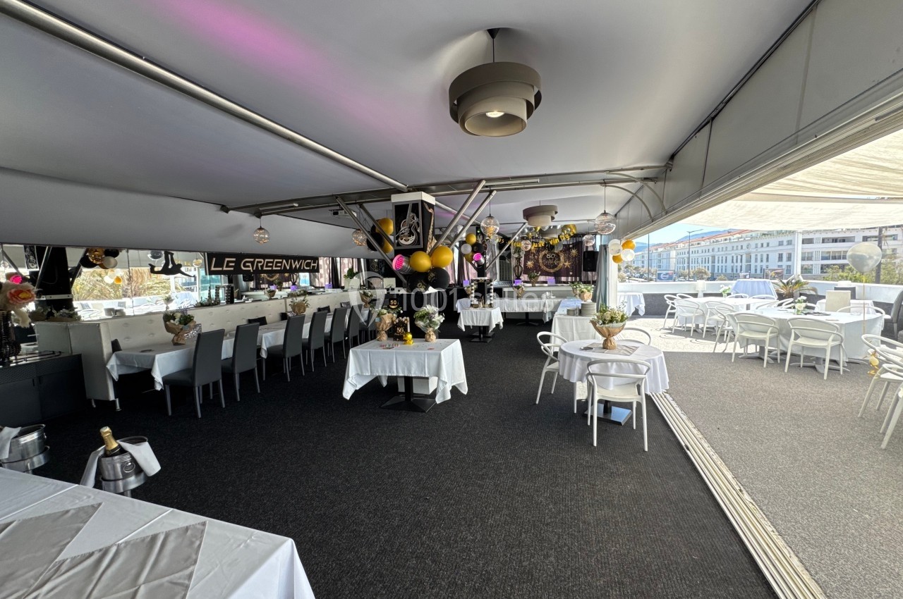 Salle de réception décorée avec des ballons et des tables dressées, ouverte sur une terrasse ensoleillée.