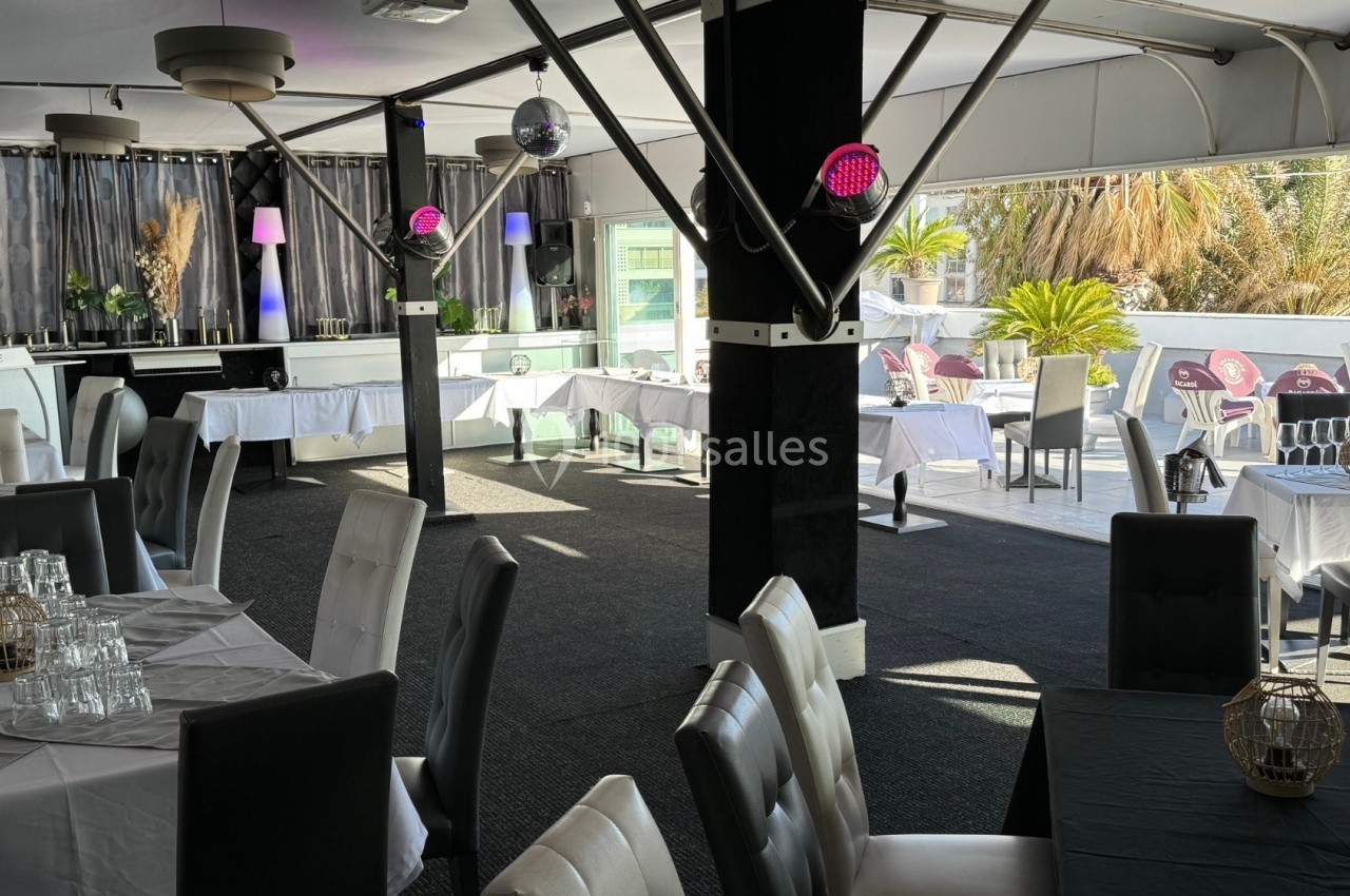 Salle de restaurant lumineuse avec tables dressées, chaises modernes et terrasse extérieure offrant une vue sur des palmiers.