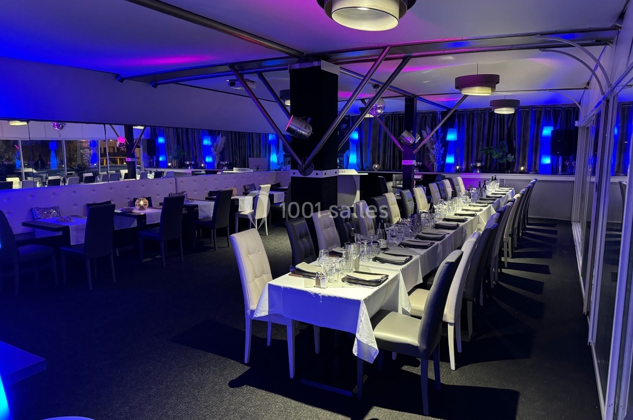Salle de restaurant élégante avec tables dressées, éclairage tamisé et ambiance lumineuse bleutée.