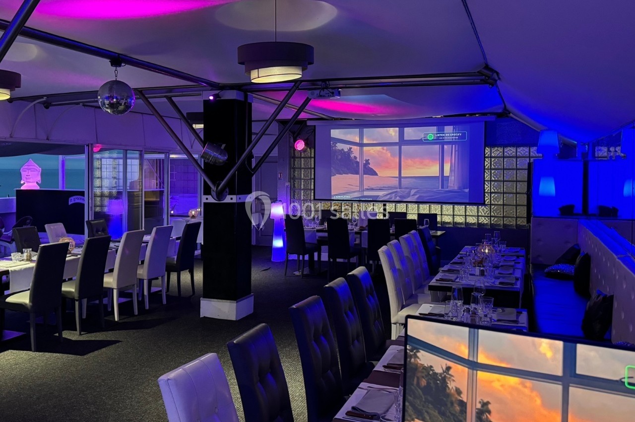 Salle de restaurant moderne avec éclairage violet, grandes baies vitrées et vue sur un coucher de soleil.