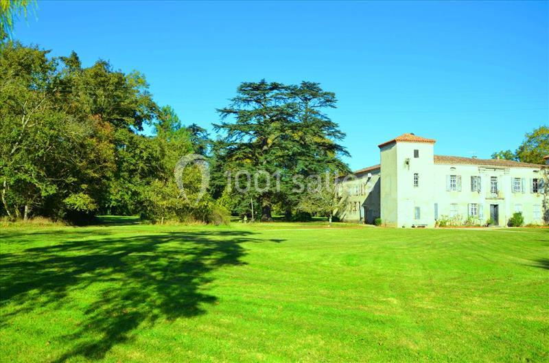 Bâtiment ancien entouré d'une pelouse verdoyante et d'arbres sous un ciel dégagé.