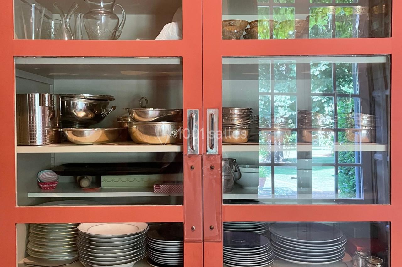 Vaisselier rouge avec portes vitrées, contenant des verres, plats, bols et assiettes en céramique et en métal.