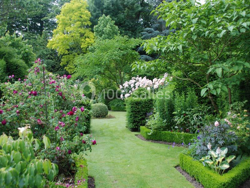 Jardin verdoyant avec allée sinueuse bordée de buissons taillés, fleurs colorées et arbres feuillus.