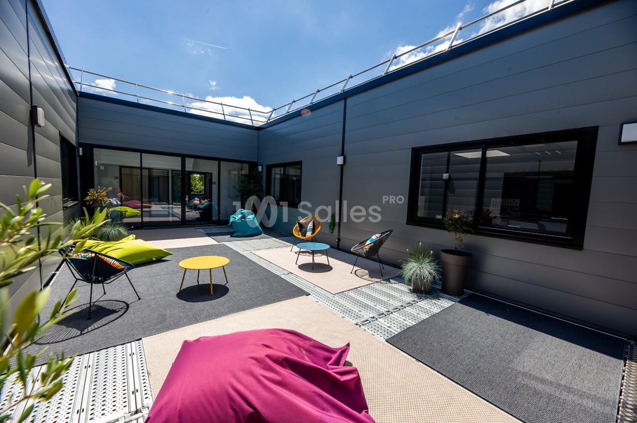 Cour extérieure moderne avec mobilier coloré, coussins, plantes en pot et revêtement de sol en dalles grises.