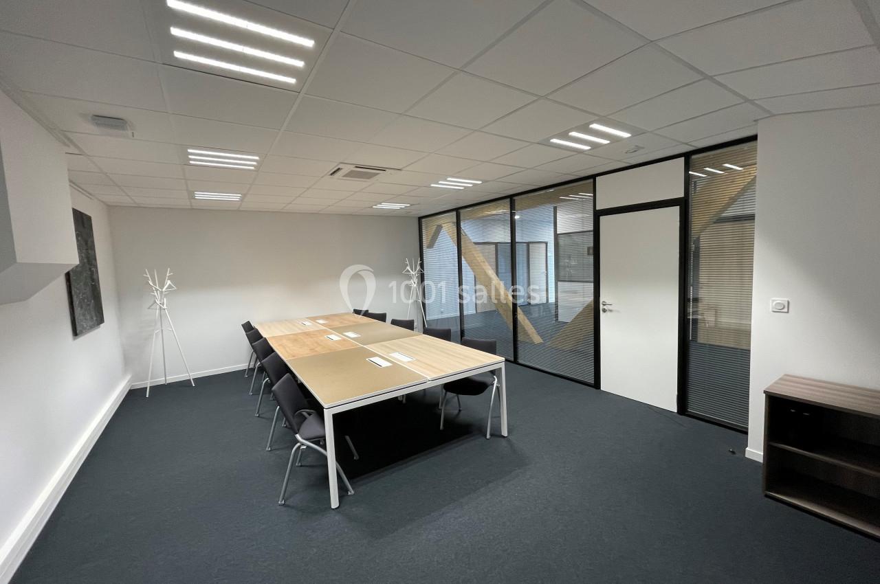 Salle de réunion lumineuse avec une grande table rectangulaire, des chaises noires et des cloisons vitrées.