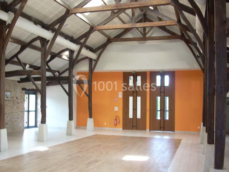Salle lumineuse avec charpente en bois apparente, murs orange et blancs, et sol en carrelage et parquet.
