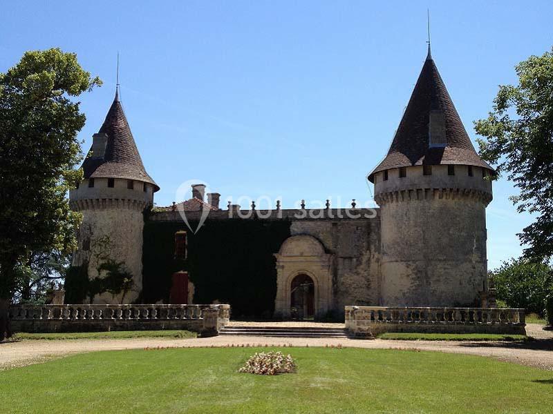 Château ancien avec deux tours rondes, entouré de verdure et d'une pelouse bien entretenue sous un ciel bleu.