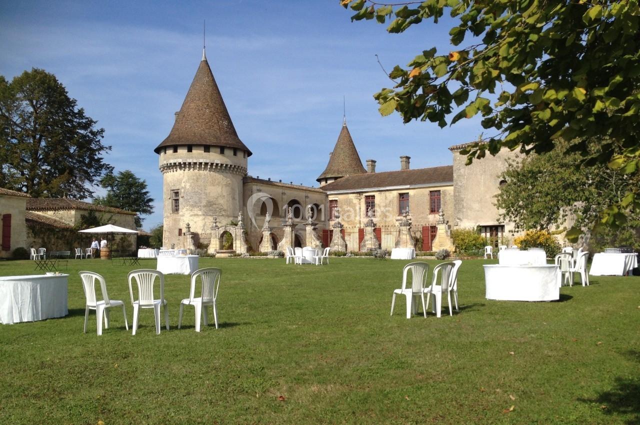 Château en pierre avec tours et pelouse aménagée de tables et chaises blanches sous un ciel dégagé.