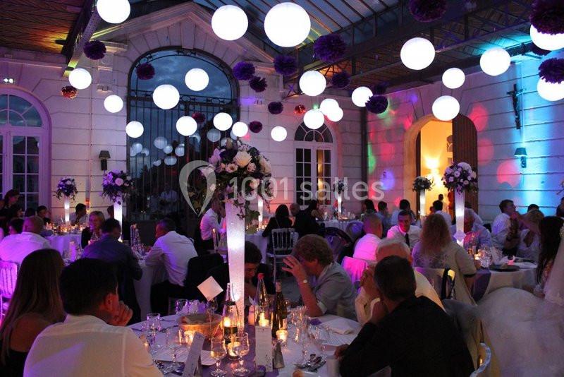Salle de réception éclairée avec des guirlandes lumineuses, des tables décorées et des invités assis lors d'un événement…