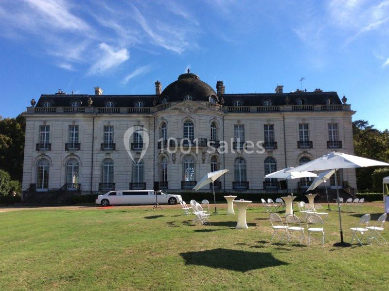 Façade d'un château blanc avec un toit mansardé, entouré d'un parc, tables et chaises installées sur la pelouse.